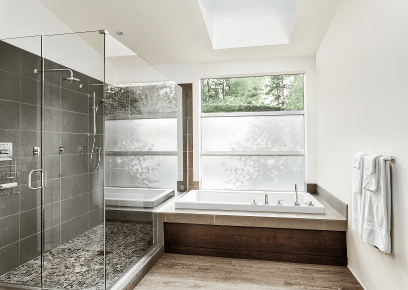 Modern bathroom with glass shower and large bathtub under skylight.
