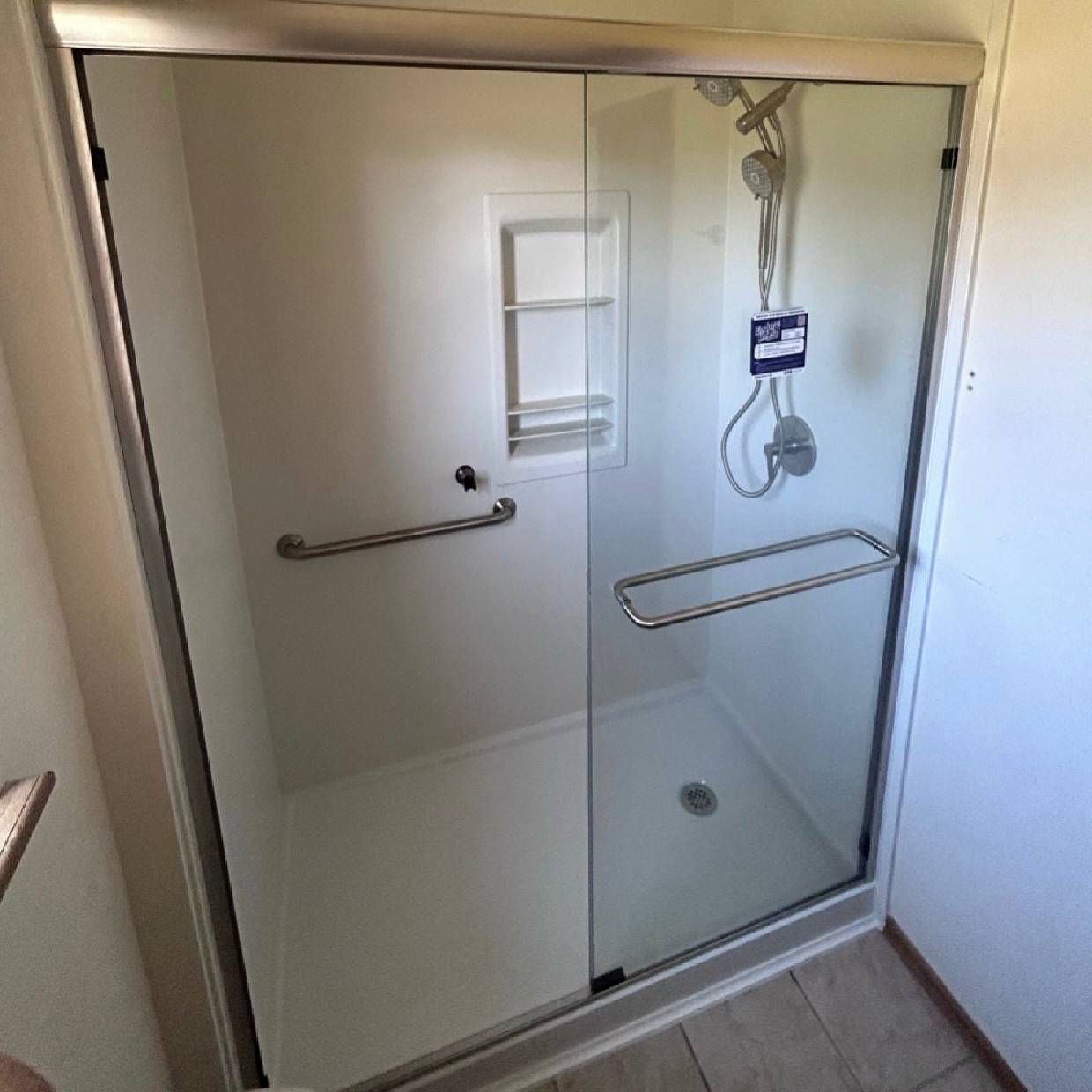 Modern glass shower door with metal handles and safety bars.