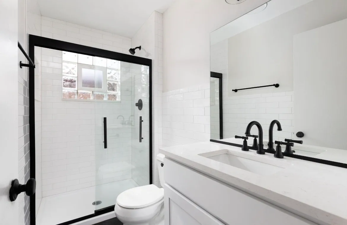 Modern white bathroom with glass shower and black fixtures.