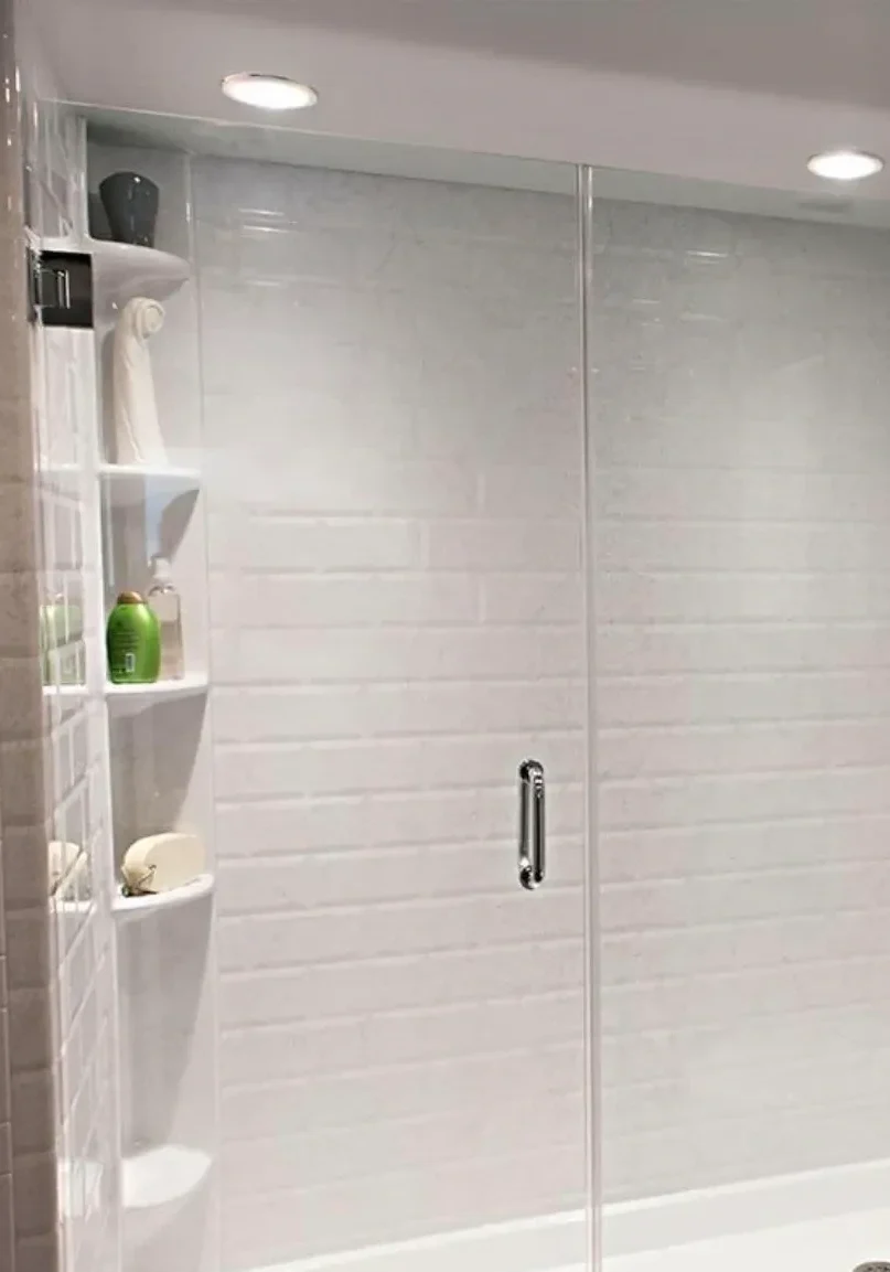 Modern glass shower enclosure with white tiles and corner shelves.