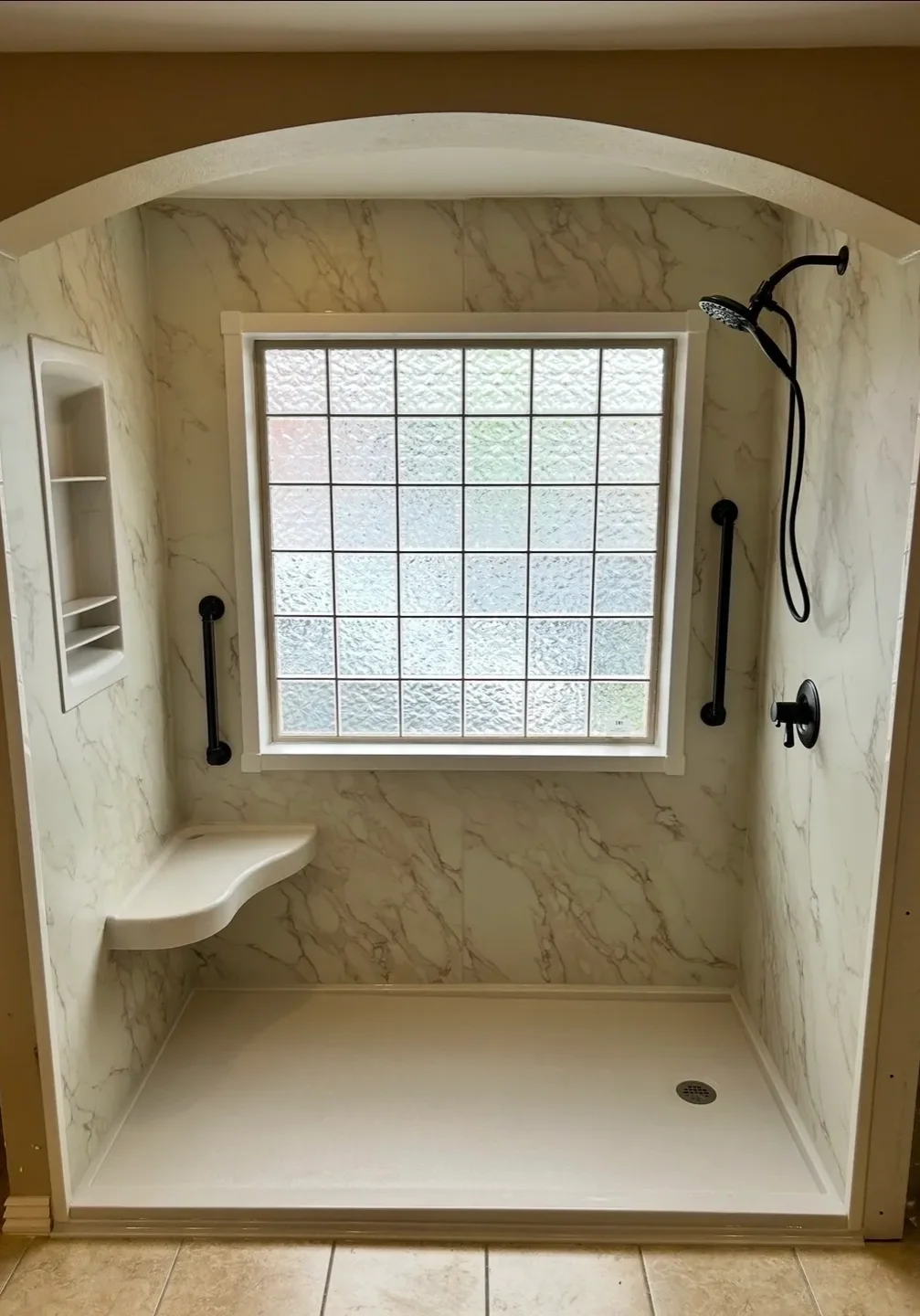 Modern shower area with marble walls and built-in bench.